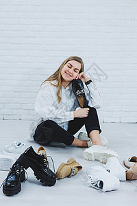 一位年轻女子坐在地板上的鞋子中间 为自己挑选新鞋 穿白衬衫和黑裤子的女士 穿白鞋的女人办公室配饰命令派对架子零售运动女性展示衣架图片