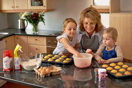 他们肯定掌握了这个……两个小女孩在家里祖母的帮助下烤纸杯蛋糕图片
