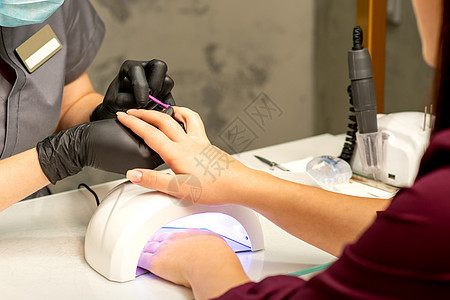 专业美甲 一位美甲师正在一家美容院用紫色指甲油为客户的女性指甲上色 特写 美容行业概念刷子搪瓷女孩抛光手套治疗紫外线工具手指凝胶图片