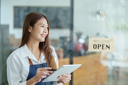 一位美丽的亚洲女性经营一家小企业的肖像 她拿着一台显示笑脸的平板电脑 一位咖啡店老板在新的早晨开店欢迎顾客 中小企业概念餐厅服务图片