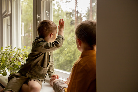 孩子们坐在窗台上等着有人来 两个兄弟 朋友 可爱的学龄前儿童独自在家 男孩们正在等待他们的母亲或父亲 孤独 忙碌的父母亲戚友情寂图片