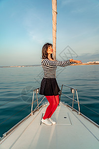 女人站在游艇的鼻子上 在阳光明媚的夏日 微风长着头发 美丽的海在背景上蓝色巡航女士海滩帆船游客娱乐闲暇派对享受图片