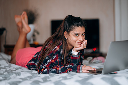 床上电脑年轻妇女在床上用笔记本电脑工作牛仔布女性眼镜卧室说谎自由职业者技术企业家博客牛仔裤背景
