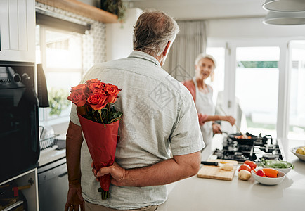 惊喜 玫瑰和一对年长夫妇在家里 浪漫的男人在家里的周年纪念日 生日或情人节那天用一束鲜花宠爱妻子 丈夫把给女人的礼物藏在身后图片