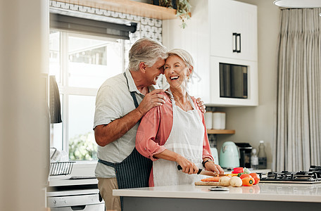 老年夫妇在厨房里 一起做健康的食物 在退休生活中快乐 老妇人围裙切菜 老白人在家抱妻爱营养晚餐图片