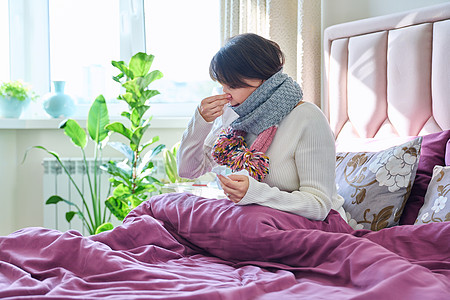 生病的妇女拿着手帕 打喷嚏 擦鼻涕 坐在家里的床上图片