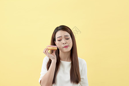 一个快乐的年轻亚洲女性 食用黄背景孤立的甜甜圈的肖像图片
