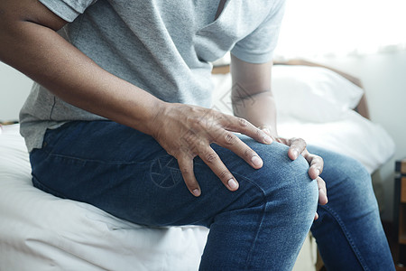青年男子在清晨坐在床上时 身受膝盖和膝部疼痛折磨的年轻男子图片