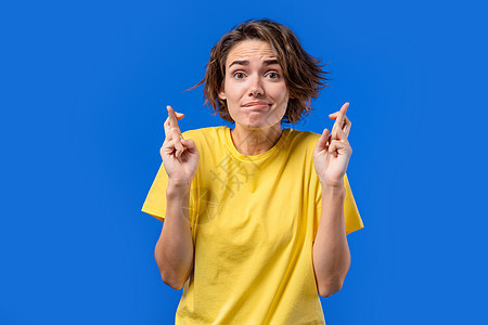 漂亮的女人在蓝色背景上用交叉的手指祈祷 女士求人满足她的欲望 帮助 祈祷她考试好运感恩希望文化宗教女性情感女孩精神信徒成人图片