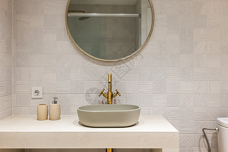 现代浴室的白色光滑大理石台面上的椭圆形时尚水槽 古铜色双阀龙头与挂在瓷砖墙上的圆镜和谐相融图片