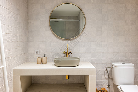 设计精美 光线明亮的浴室采用柔和的色彩 点缀着明亮的铜色金属细节 玻璃隔断的淋浴区映照在墙上的圆镜中背景图片