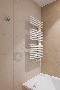 中央浴室的一角 墙上有一个白色的暖气片 用来晾干毛巾 房间的墙壁上铺着不同颜色的米色瓷砖 纯白色亚克力浴缸图片