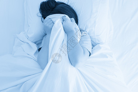 女人把脸藏在床上的毯子下羽绒黑发卧室说谎枕头头发就寝床单苏醒寝具图片
