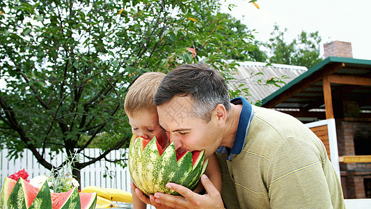 夏天 在花园里 父亲带着四岁的儿子切西瓜吃 玩得很开心 一个男孩非常喜欢西瓜 与家人共进午餐的甜西瓜孩子女性营养白色姐姐动作快乐图片