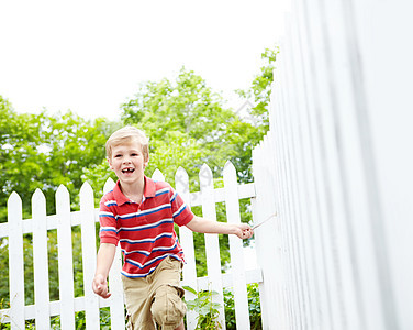 一个可爱的小男孩在后院的白色栅栏上 拿着棍子跑来跑去图片