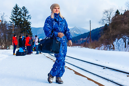 穿着冬衣的年轻女子在等火车假期靴子铁路时尚女性头发案件旅行金发铁轨图片
