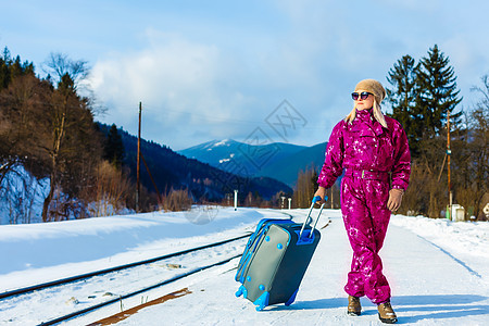 穿着冬衣的年轻女子在等火车铁轨靴子潮人时尚车站成人背包围巾手提箱金发图片