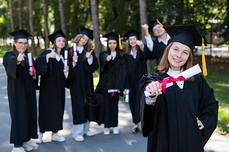 中学学校一群在户外穿毕业礼服的快乐学生 一个年轻女孩 她手上拿着文凭 在前台仪式幸福同学教育庆典喜悦帽子学校中学研究生背景