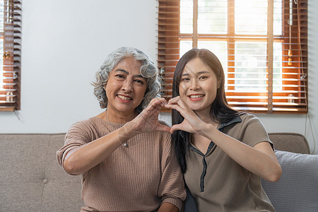 慈爱的成年女儿在家里的沙发上拥抱年长的母亲 家人一起享受温柔的时刻 年轻女性和成熟的妈妈或祖母相望 两代人快乐乐趣女孩退休幸福父图片