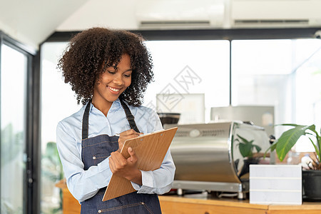 身着围裙的年轻非裔女服务员 准备接受客户订购的肖像生意微笑企业家服务业成人女性标志咖啡师职业服务图片
