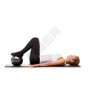 锻炼是她日常生活的一部分 一名年轻女子躺在她的运动垫上时使用健身球 - 与世隔绝图片