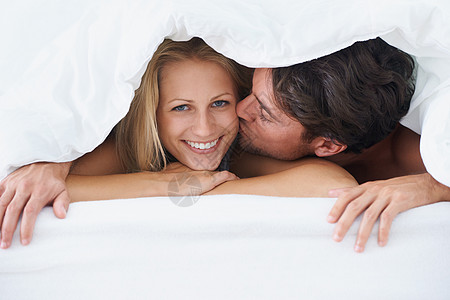 和老公在一起很开心 一个男人躺在床上 依偎在被套下 亲吻一个微笑的女人的脸颊图片