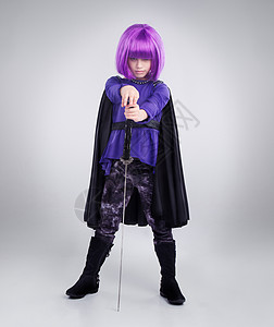 小女孩 超级英雄和万圣节装扮在灰色工作室背景下用剑摆姿势 扮演超级英雄的女童肖像 紫色头发 服装或武士义警的角色扮演图片