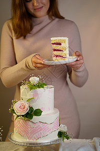 女孩切开并端上一块蛋糕 灰色背景中用鲜花装饰的喜庆婚礼两层蛋糕生日美食白色庆典绿色花朵派对奶油粉色玫瑰图片