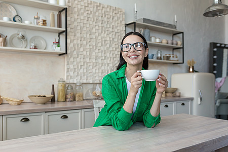 有个年轻女人在家喝咖啡 休息一会 他手里握着杯子 望窗外看图片