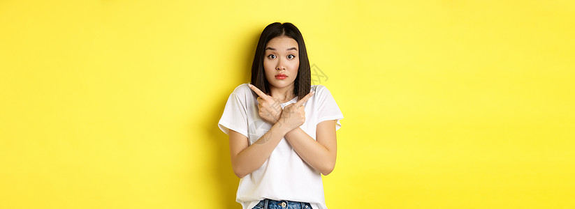 麻木不仁的亚洲女孩需要帮助选择 指指手指侧面和看不清 站在黄色背景上站立成人发型情感广告青少年工作室理发促销女性商业图片