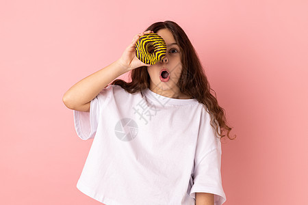 兴奋的小女孩站着玩得开心 拿着甜甜圈遮住眼睛 张开嘴图片