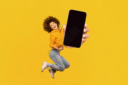 快乐的女士在空中跳跃 用智能手机手握 显示空展示升迁图片
