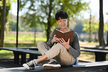 年轻亚洲男子学生在市公园坐在长椅上时读有趣的书 阅读有意思的书;教育 生活方式概念图片