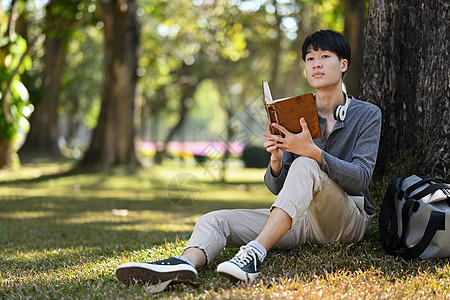 年轻亚洲人学生在读有趣的书 在城市公园的绿色草地上欢乐地花时间玩乐图片