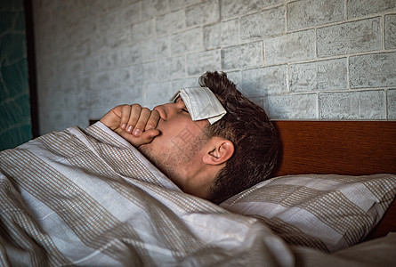 年青英俊的生病或病倒在床上患感冒或发烧的男人图片