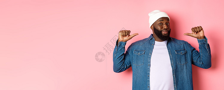 自信和冷酷的黑人男子指着自己 盯着相机自我确定 炫耀 站在粉红背景上快乐胡须横幅促销情感冒充胡子广告衬衫帽子背景图片