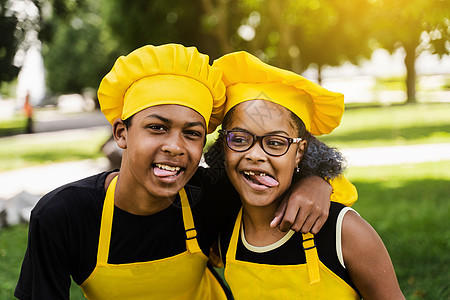 身着黄色制服和厨师帽的非洲儿童做着鬼脸 互相吐舌头 非洲少年和黑人女孩玩得开心 做饭童年厨房烹饪朋友们面包师兄弟围裙帽子家庭乐趣图片