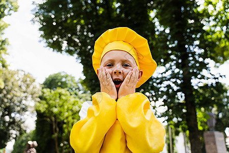 穿着黄色厨师帽子和围裙穿黄色制服的厨艺儿童被吓得脸颊惊呆 在户外出人意料童年活动公园面包师乐趣食物男生厨房孩子们面包图片