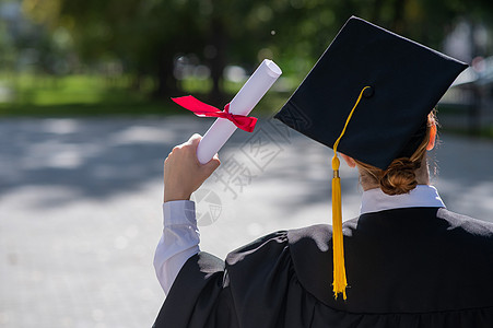 毕业学士在户外持有文凭的女毕业生礼服上看到一位天主教妇女背景