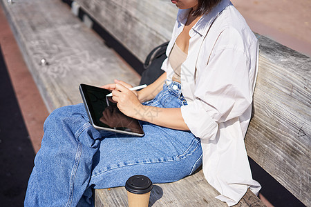 女性手握笔 在数字平板电脑上抽取 坐在公园的长凳上图片
