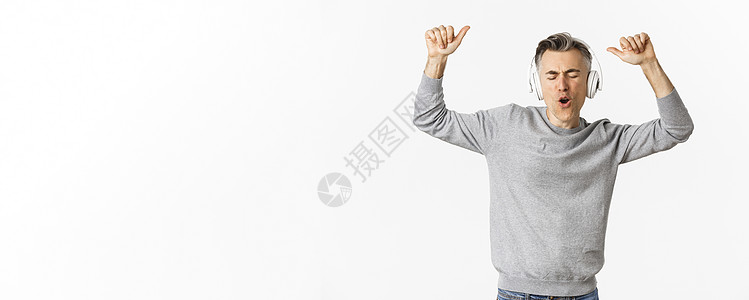 英俊 现代中年男子的肖像 耳机和舞蹈播放音乐 站在白色背景上 笑声幸福商业男性毛衣快乐成人广告促销发型情感背景图片