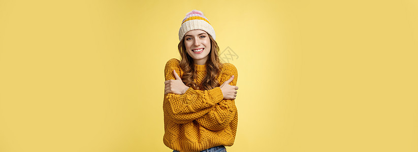 冷了带上外套 肖像迷人温柔女性可爱的女朋友拥抱自己拥抱微笑温暖的凝视站在外面站着针织毛衣帽 黄色背景欢呼毛衣快乐新年成人派对发型图片