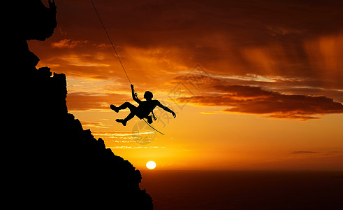日落天空绳降 山的轮廓和徒步旅行的人挂在影子绳上 健身风险 冒险自由挑战和强烈 超现实的自然肾上腺素和在橙色景观上攀登悬崖图片