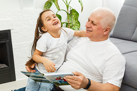 快乐的小女孩和爷爷在家读故事书的小女儿在一起孩子微笑幸福童年祖父母关爱男性孙女男人孙辈图片