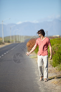 一个年轻人在一条废弃的路上走着搭便车 想搭个顺风车呢 笑声男性假期天空冒险闲暇远足货车旅行游客吉普车背景图片