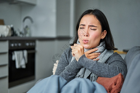 红肿过敏生病的韩国妇女咳嗽和感觉不舒服 严酷 有流感 感冒或流感 呆在家中互联网发烧长椅房子疼痛过敏鼻子沙发女性药品背景