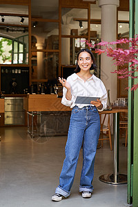 站在咖啡厅入口前的女服务员 向餐厅里带平板电脑的宾客邀请一对餐饮客人经理食堂工作横幅人士商业自雇咖啡成人技术图片