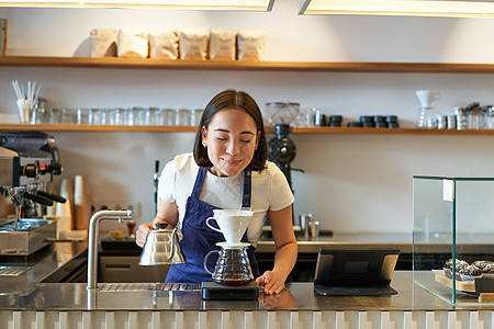 微笑的亚洲女孩一边冲泡过滤器一边闻着咖啡的味道 站在咖啡馆的柜台后面图片