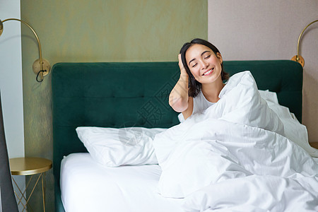 快乐的韩国女人在酒店房间醒来 躺在舒适温暖的毯子和白色床单下的床上 享受周末的早晨小憩女性成人就寝时间枕头房子女孩午睡女士图片