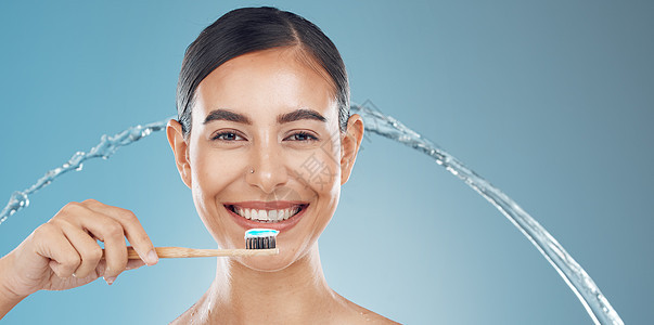 女人在淋浴时在蓝色背景下刷牙 水溅和健康 牙齿清洁和口腔化妆品 快乐的年轻模特脸像 牙刷上的牙膏和健康的牙齿微笑图片